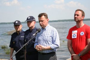 minister Mariusz Błaszczak przemawia stojąc w towarzystwie dwóch policjantów i jednego ratownika wodnego