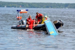dwóch ratowników na łodzi ratunkowej wyciąga z wody osobę, która się topiła