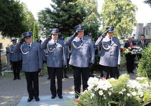 grupa czterech policjantów stoi przed grobem i oddaje honor, w tle stoi kilku policjantów i zaproszeni goście
