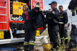strażacy pomagają założyć strój strażacki kierowcy biorącemu udział w akcji