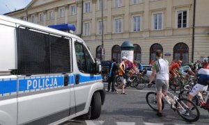 policyjny radiowóz, w tle grupa kolarzy wyścigu Tour  de Pologne