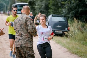 uczestnicy ultramaratonu biegnący kobieta i mężczyzna oraz stojący tyłem żołnierz
