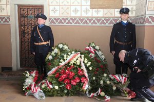 policjanci w mundurach historycznych stoją pod tablicą pamiątkową, po środku wieńce i kwiaty