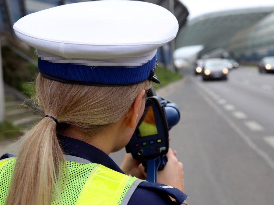 policjantka ruchu drogowego kontroluje prędkość trzymając w ręku miernik prędkości - widok z tyłu