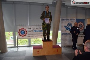 zawodnik ubrany w wojskowe moro stoi na podium trzymając dyplom i puchar