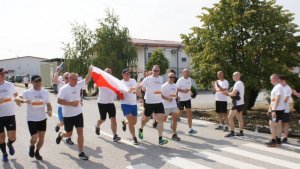 grupa mężczyzn biegnących w strojach sportowych jeden z nich trzyma polska flagę