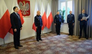 policjanci uczestnicy uroczystości stoją na tle flag polski