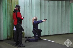 policjantka strzela w pozycji klęczącej, instruktor obserwuje z tyłu