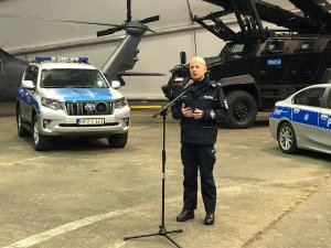 Komendant Główny Policji przed mikrofonem, z tyłu sprzęt zakupiony w 2019 roku - transporter opancerzony i fragmenty dwóch oznakowanych radiowozów