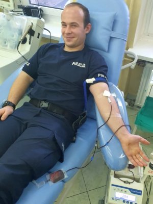 Uśmiechnięty policjant na fotelu w centrum krwiodawstwa.