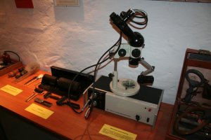 Na stole stoi mikroskop stereoskopowy z lat siedemdziesiątych produkcji polskich zakładów optycznych w warszawie.