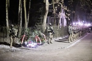 Pomnik upamiętniający poległych policjantów w Magdalence ze złożonymi wieńcami, widoczna warta honorowa oraz funkcjonariusze z palącymi się pochodniami