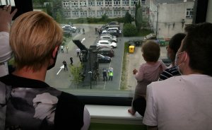 Dzieci i personel medyczny patrzący przez okno szpitala na pokaz policjantów.