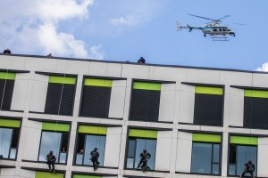 Policyjni kontrterroryści podczas schodzenia po linach z dachu szpitala, w tle policyjny śmigłowiec Bell 407.