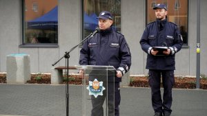 Komendant Policji w Pile stoi za mikrofonem na statywie, za nim widać umundurowanego policjanta