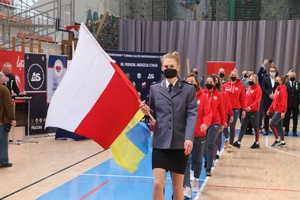 policjantka niesie flagę biało-czerwoną, za nią idzie kobiecy zespół biorący udział w turnieju