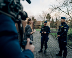 dwoje policjantów na chodniku rozmawia z kobieta, z przodu widać operatora kamery