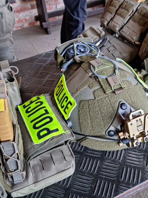 Metalowy stół, na nim hełm taktyczny i kamizelki w kolorze khaki, w kieszeniach kamizelek magazynki z amunicją.