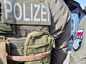 Zdjęcie pleców funkcjonariusza niemieckiej policji ubranego w mundur taktyczny z napisem Polizei plecach, obok ramię polskiego funkcjonariusza z naszywką BOA i flagą Polski.