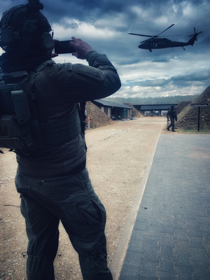 Teren ośrodka szkoleniowego. Funkcjonariusz w umundurowaniu taktycznym wykonujący zdjęcie przelatującemu śmigłowcowi Black Hawk.
