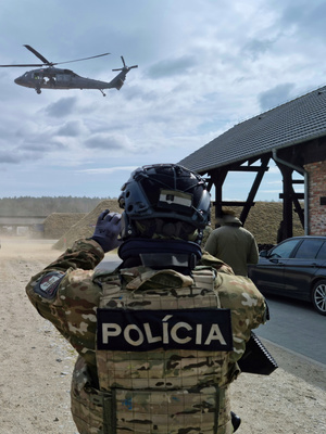 Teren ośrodka szkoleniowego. Funkcjonariusz w umundurowaniu taktycznym wykonujący zdjęcie przelatującemu śmigłowcowi Black Hawk.
