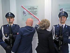 Komendant Główny Policji i kobieta z rodziny zmarłej Marii Czernek zrywają biało czerwona szarfę z tablicy jej imienia