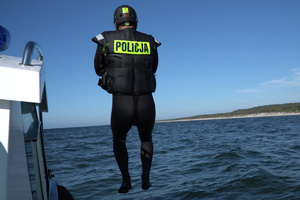 Policyjny ratownik w kombinezonie do pływania w trakcie skoku do wody z pokładu łodzi.