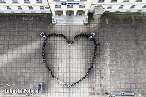 Policjanci i pracownicy cywilni stoją przed budynkiem komendy tworząc kształt serca - widok z góry.