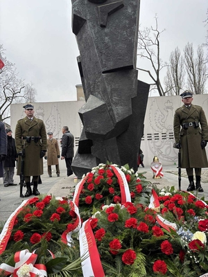Wieńce złożone pod pomnikiem. Obok żołnierze na warcie.