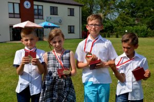 czworo nagrodzonych dzieci (trzej chłopcy i dziewczynka) stoją i pokazują otrzymane medale