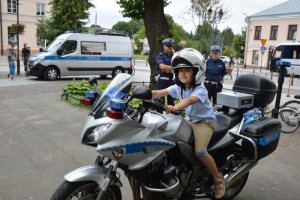 Wojewódzkie obchody Święta Policji w Krasnymstawie, chłopiec na policyjnym motocyklu w tle dwaj policjanci