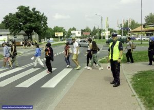 młodzi pielgrzymi przechodzący na pasach przez drogę i policjant pilnujący porządku