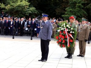 uroczystości ku czci poległych i walczących o Warszawę w 1944 roku, uroczystości przed pomnikiem Polskiego Państwa Podziemnego i Armii Krajowej przy ul. Wiejskiej, policjant oddaje honor, za nim stoi delegacja wojska polskiego