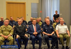 Wiceminister Jarosław Zieliński siedzi w towarzystwie szefów służb biorących udział w zabezpieczeniu Światowych Dni Młodzieży na spotkaniu w MSWiA w tle siedzą policjanci i żołnierze