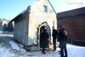 Młodszy aspirant Michał Mamoń ogląda starą kapliczkę znajdującą się na jednej z lędzińskich posesji w towarzystwie kilku osób