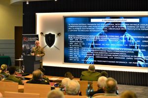 Funkcjonariusz stojący przy mównicy przemawia do zebranych na sali osób.