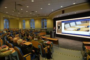 Funkcjonariusz stojący przy mównicy przemawia do zebranych na sali osób.