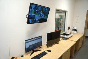 zdjęcie pokoju, w którym znajdują się meble, monitory, krzesło oraz specjalne okno z widokiem na poczekalnie