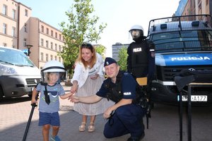 rodzina z dzieckiem przy stoisku policyjnym , maluch zakłada kask ochronny , obok policjant.