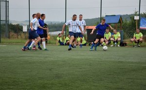 Fotografia kolorowa przedstawiająca rywalizację drużyn piłkarskich na boisku.