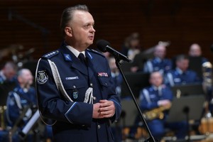 Zdjęcie przedstawia policjanta w mundurze galowym mówiącego do mikrofonu