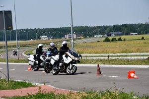 Trzech policjantów na motocyklach pokonuje slalom między pachołkami.